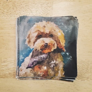 May include: A stack of fabric squares with a painting of a small, light brown dog wearing a purple bandana. The dog is looking directly at the camera. The background is a blue and gray watercolor wash.