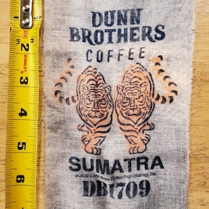 May include: A white fabric coffee bag with a black and orange tiger design. The bag has the text "Dunn Brothers Coffee" and "Sumatra" printed on it. The bag also has the text "DB1709" printed on it.