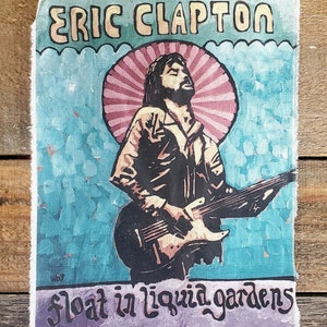 May include: A vintage-style poster featuring Eric Clapton playing a guitar. The poster has a blue background with a pink and white sunburst behind Clapton. The text "float in liquid gardens" is at the bottom of the poster.