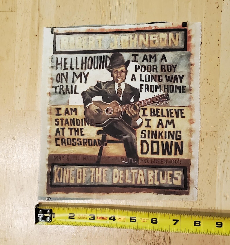 Pu&ograve; includere: Un'opera d'arte quadrata in tessuto con un dipinto di Robert Johnson che suona la chitarra. Il testo include "Hellhound on my Trail" e "King of the Delta Blues". Il pezzo misura circa 15 cm di larghezza.