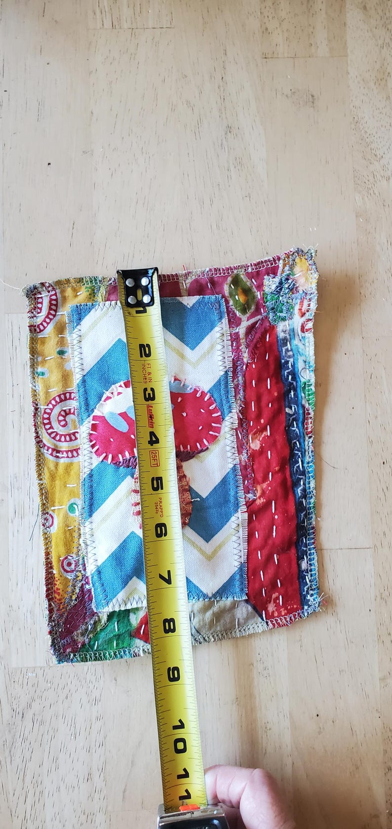 May include: A colourful, handmade fabric square with a patchwork design. The square features various patterns, including a blue and white chevron, red strawberry shapes, and yellow floral fabric. The square is approximately 20 cm long.