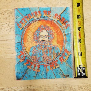 May include: A blue and orange patch with the text "Let There Be Songs To Fill The Air" and a portrait of a man with long hair and a beard.