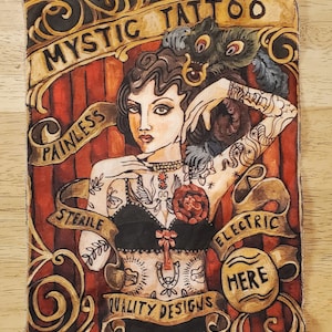 May include: A fabric art piece with a vintage illustration of a woman with tattoos. The artwork includes the text "Mystic Tattoo" and other phrases. The colour palette includes red, brown, and gold.