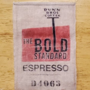 May include: A white fabric tag with red and black text. The tag reads "Dunn Bros Coffee The Bold Standard Espresso 04063".