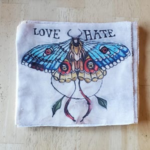 May include: A white canvas tote bag with a blue, yellow, and red butterfly illustration and the words "LOVE HATE" printed on the front.