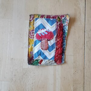 May include: A handmade fabric patch with a mushroom applique. The patch features a red mushroom with a white and blue chevron pattern, and is bordered by various patterned fabrics.