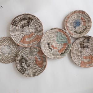 Puede incluir: Un conjunto de seis cestas de pared redondas tejidas etiquetadas como Set A. Cada cesta presenta un dise&ntilde;o en espiral en tonos neutros con acentos en terracota, negro, azul verdoso y azul. Las cestas var&iacute;an en tama&ntilde;o y patr&oacute;n.