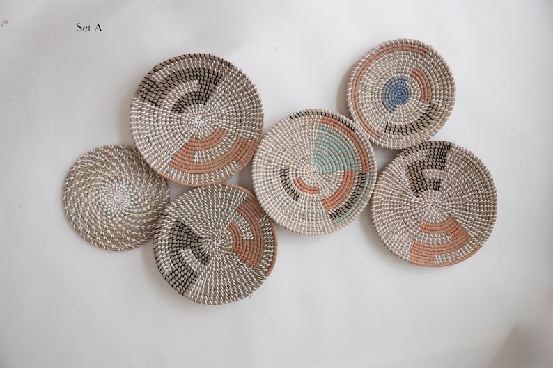 Puede incluir: Un conjunto de seis cestas de pared redondas tejidas etiquetadas como Set A. Cada cesta presenta un dise&ntilde;o en espiral en tonos neutros con acentos en terracota, negro, azul verdoso y azul. Las cestas var&iacute;an en tama&ntilde;o y patr&oacute;n.