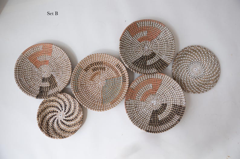 Puede incluir: Un conjunto de seis cestas de pared redondas tejidas etiquetadas como Set B. Las cestas presentan dise&ntilde;os en espiral en tonos neutros de beige, blanco, terracota y marr&oacute;n oscuro, con varios patrones geom&eacute;tricos tejidos en fibra natural.
