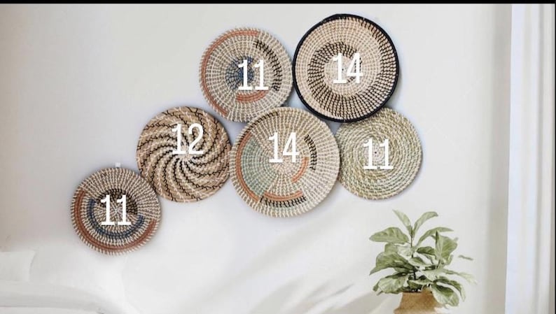 Puede incluir: Una colecci&oacute;n de seis cestas de pared tejidas redondas con fibras naturales en tonos bronceado, marr&oacute;n, negro y azul verdoso apagado. Las cestas est&aacute;n dispuestas en grupo, cada una marcada con un n&uacute;mero blanco 11, 12 o 14, con espirales.