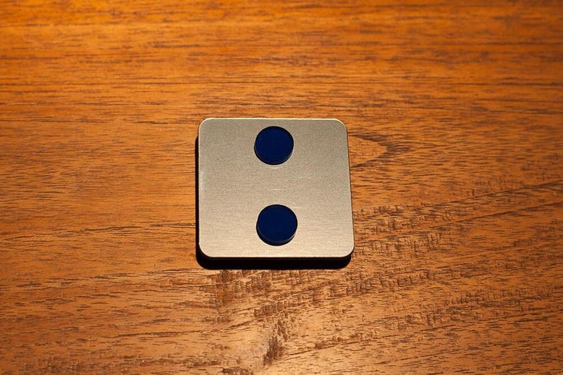 May include: A square, brushed metal object with two evenly spaced, circular, dark blue insets. The object is set against a warm, wooden background.