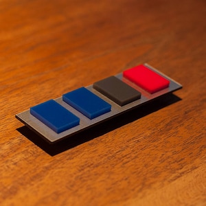 May include: A silver metal bar with four colored rectangular buttons. The buttons are blue, blue, gray, and red.