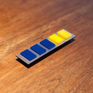 May include: A silver metal bar with six rectangular buttons. The buttons are blue and yellow, arranged in a gradient pattern.