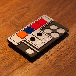 Puede incluir: Un panel de control plateado y negro con cinco botones rojos, naranja y azules, dos botones redondos negros y cinco botones redondos plateados.