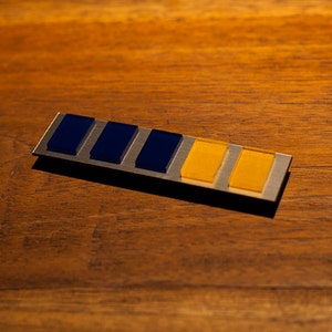 May include: A silver metal bar with five rectangular blue and yellow glass inserts. The bar has a smooth, polished surface.