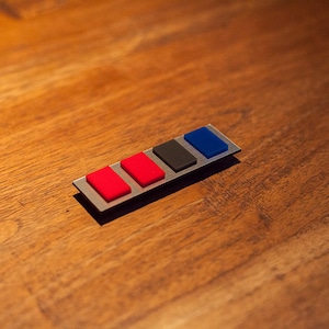 May include: A silver metal bar with five colored buttons. Two red buttons, one black button, and two blue buttons.