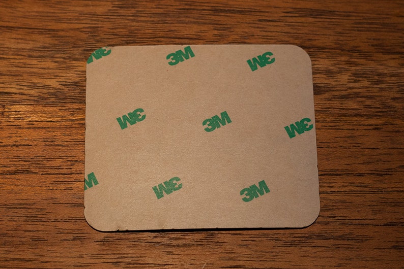 May include: A brown square adhesive sheet with the 3M logo printed in green on it.