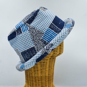 Può includere: Un cappello con motivo blu e bianco con un design geometrico. Il cappello è su un supporto per cappello in vimini.