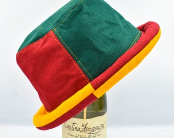 May include: A colorful, patchwork hat with a square crown and a wide brim. The hat features panels of red, green, and yellow fabric, stitched together with yellow thread. The brim is lined with yellow fabric.