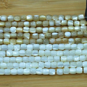 May include: Multiple strands of square-shaped beads arranged in rows. The top rows feature beads with a tan and cream iridescent finish, while the bottom rows consist of beads with a bright white, pearlescent, and smooth polished surface.