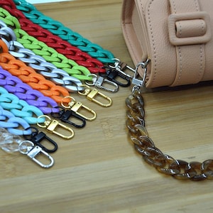 May include: A set of colorful plastic chain bag straps with silver and gold clasps. The straps are in various colors, including green, red, orange, purple, and blue. A brown plastic chain strap is also included.