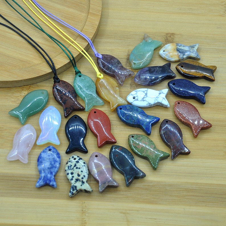May include: A collection of 20 gemstone fish pendants, each carved from a different type of stone. The pendants are displayed on a wooden surface with a variety of colors and patterns.