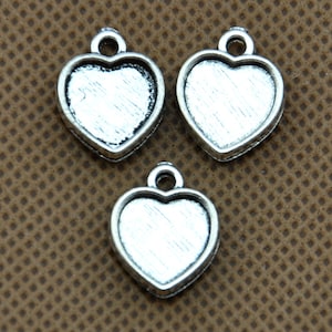 May include: Three silver heart-shaped pendant charms with a smooth, slightly textured surface. The charms have a loop at the top for attaching to a necklace or bracelet.