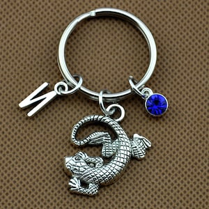 Puede incluir: Llavero de plata con un dije de lagarto, un dije de cristal azul y un dije de letra 'N'.