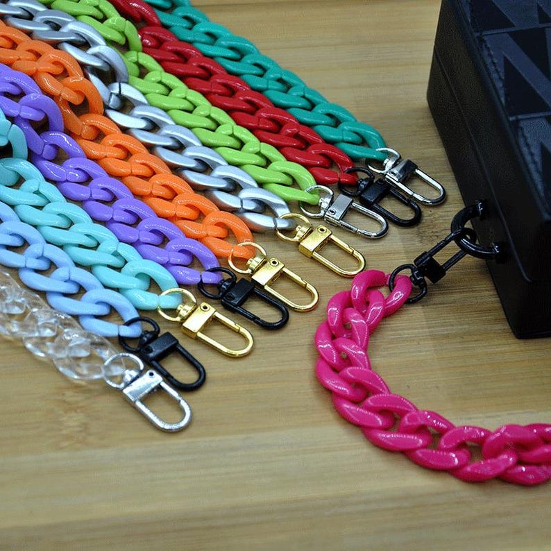 May include: Assortment of colorful plastic chain bag straps with gold and black clasps. The chains are in various colors including clear, light blue, lavender, orange, lime green, silver, red, and teal.