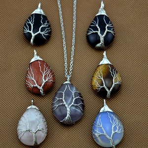May include: Seven silver wire wrapped tree of life pendants with different colored stones. The stones are black, red, brown, purple, pink, and blue.
