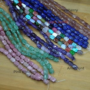 May include: A selection of gemstone beads in shades of pink, green, purple, and blue. The beads are strung, with labels identifying them as Pink Rhodonite, Green Aventurine, Amethyst, and Lapis Lazuli. The word "Mixed" is also visible.