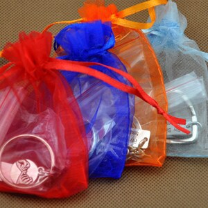 May include: Three organza gift bags in red, blue, and light blue with silver jewelry inside. The bags are tied with matching ribbons.