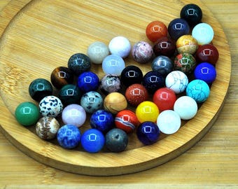 May include: A collection of 30 colourful gemstone beads, each approximately 1 cm in diameter. The beads are arranged in a circular pattern on a wooden surface. The beads are a variety of colours, including red, blue, green, yellow, and brown.