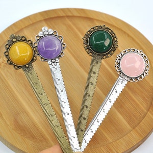 May include: Four decorative metal bookmarks with rulers. Each bookmark features a different colored glass cabochon in a silver or bronze setting. The cabochons are yellow, purple, green, and pink.