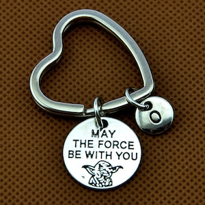 Peut inclure: Porte-clés en forme de cœur argenté avec un charme rond qui dit "Que la Force soit avec toi" et représente une image de Yoda. Le charme est attaché à un plus petit charme rond avec la lettre "O" dessus.