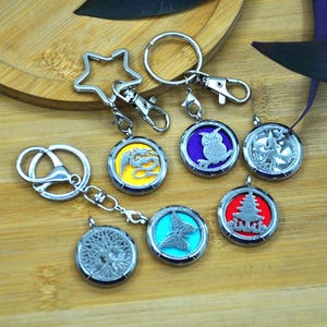 Peut inclure: Six porte-clés argentés avec différents pendentifs. Chaque pendentif est un médaillon rond avec un motif différent. Les motifs comprennent un dragon, un hibou, un papillon, un arbre, une pagode et un motif floral. Les porte-clés sont sur une surface en bois.
