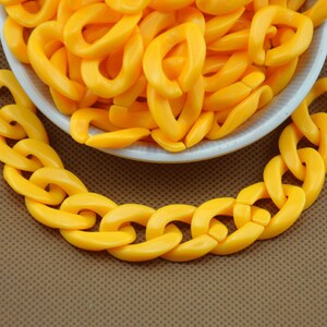 Pode incluir: Uma tigela cheia de elos de corrente de plástico amarelo brilhante. Os elos da corrente medem aproximadamente 2,5 cm de comprimento e têm uma superfície lisa e arredondada.
