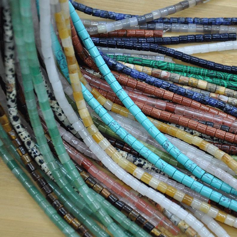 May include: Assortment of colorful gemstone beads, including turquoise, green, brown, white, and red. The beads are all square shaped and strung on a string.