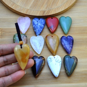 May include: A collection of 12 heart-shaped pendants made from various types of polished stones, including rose quartz, blue lace agate, red jasper, green aventurine, clear quartz, citrine, amethyst, tiger's eye, white howlite, and green aventurine.