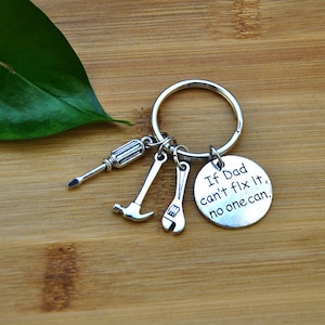 May include: Silver keychain with a round charm that says "If Dad can't fix it, no one can." The charm is attached to a silver key ring with three small silver charms shaped like a screwdriver, hammer, and wrench.