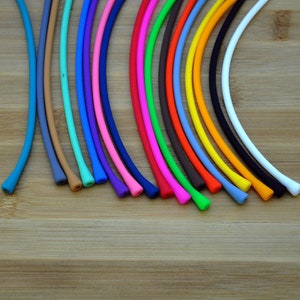 May include: A collection of thin, flexible, cylindrical silicone cords arranged in a fan pattern. The cords are available in a variety of solid colors including blue, tan, teal, purple, pink, dark blue, red, green, brown, orange, yellow, black, and white.