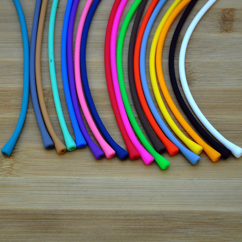 May include: A collection of thin, flexible, cylindrical silicone cords arranged in a fan pattern. The cords are available in a variety of solid colors including blue, tan, teal, purple, pink, dark blue, red, green, brown, orange, yellow, black, and white.