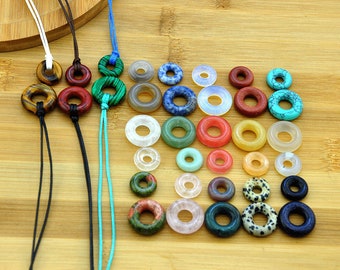May include: Assortment of colorful gemstone rings, some with a natural stone pattern, on a wooden surface. The rings are strung on cords of various colors.