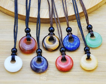 May include: Eight necklaces with round gemstone pendants. The pendants are in various colors, including white, red, orange, yellow, green, blue, and purple. The necklaces are made with black cord and black beads.