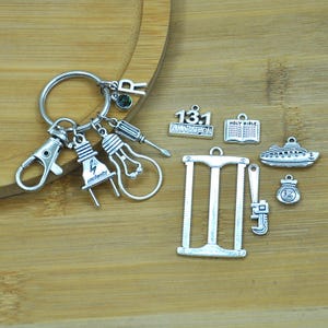 Puede incluir: Un brazalete de plata con varios dijes, incluyendo una bombilla, una llave inglesa, una sierra, un barco, una biblia y un dije con el número "131".