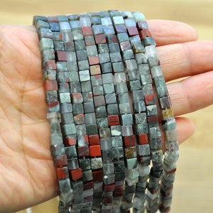 Puede incluir: Una hebra de cuentas cuadradas hechas de jaspe rojo, verde y blanco. Las cuentas miden aproximadamente 6 mm.