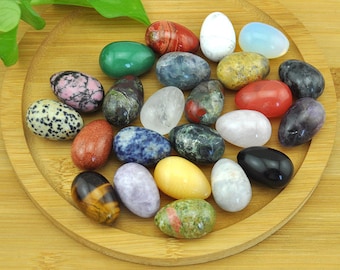 May include: A collection of 20 smooth, polished gemstone eggs in various colors and patterns, including green, red, white, black, and brown. The eggs are arranged on a wooden plate.