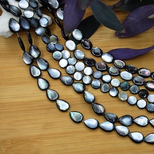 May include: Multiple strands of iridescent black and silver mother-of-pearl beads in teardrop and circular shapes. The beads exhibit a natural luster with subtle flashes of green and purple, strung together to form long, flowing jewelry components.
