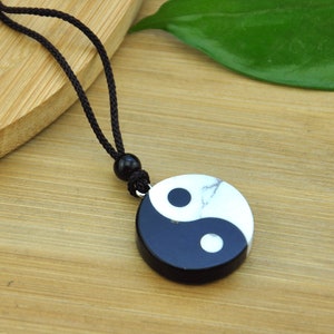 May include: A black and white yin yang pendant necklace with a black cord. The pendant is made of stone and has a marbled effect.