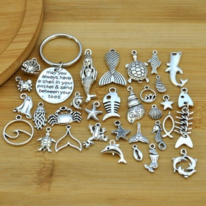 May include: A silver charm keychain with a round charm that reads "may you always have a shell in your pocket & sand between your toes". The keychain also includes a variety of silver charms with sea-themed designs, including mermaids, fish, seashells, starfish, and crabs.